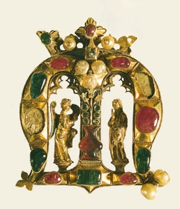 Gothic Founder's Jewel. A gold crowned M adorned with rubies, emeralds, pearls, enamelling and gothic details in the archs that serve as shrine spaces for the Angel of Annunciation and the Virgin Mary.
